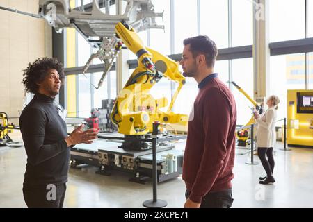 Two engineers discuss a sophisticated robotic arm used for industrial automation and manufacturing processes in a high-tech production facility. Stock Photo