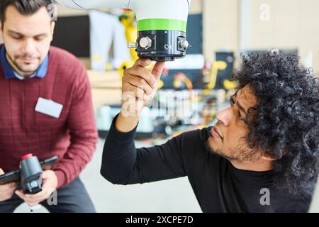 Two engineers collaborate on programming and inspecting a robotic arm in an industrial environment, showcasing modern automation and technology. Stock Photo