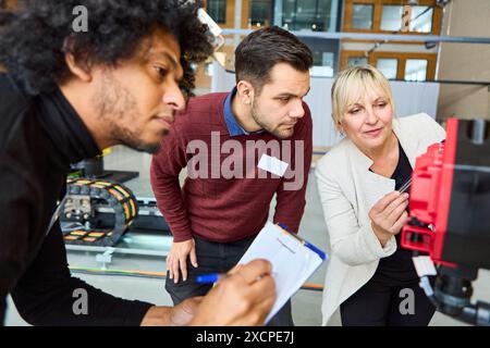 Group of engineers working together on programming and inspecting a robot with gripper arms at an industrial manufacturing facility. Stock Photo