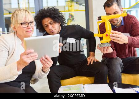 Team of professionals collaborating on robotics development using a tablet and a robot model in an office setting. Stock Photo