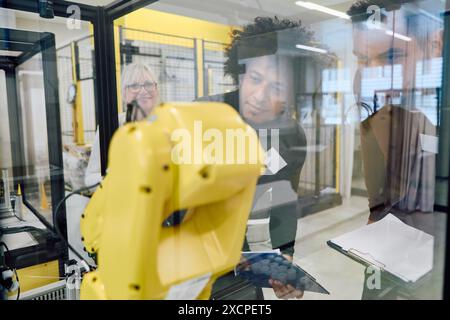 Team of engineers working together to program and inspect a robotic arm inside an industrial facility. Concepts of technology, teamwork, and process a Stock Photo