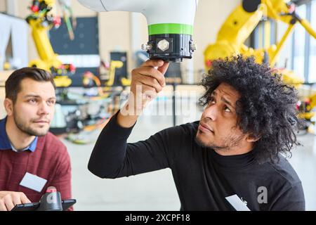 Engineers examining and programming a robotic arm in an industrial environment. Focus on robotics, automation, and industry. Stock Photo