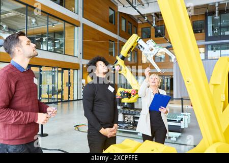 Team of engineers collaborating and training on programming a robotic arm for automation in a modern industrial facility. Stock Photo