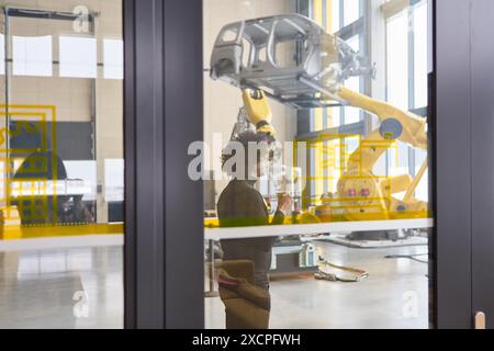 Engineer in a modern robotics lab working on programming and inspecting robotic arms used for production and process automation. Stock Photo