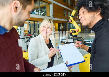 Group of professionals reviewing plans for a robotics project with a robotic arm in the background in a modern industrial setting Stock Photo