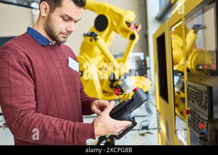 Engineer working on programming an industrial robot with a gripper arm in a factory setting, focusing on automated production and robotics technology. Stock Photo