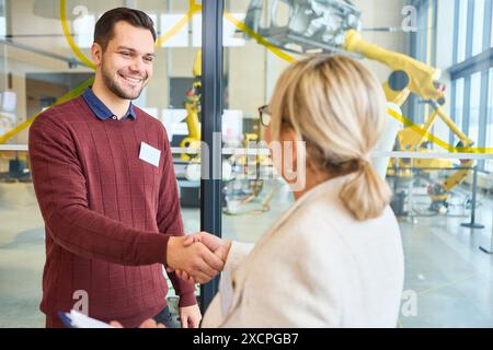 Business professionals shaking hands at a robotics training facility, highlighting technology and industrial automation. Background shows robotic arms Stock Photo