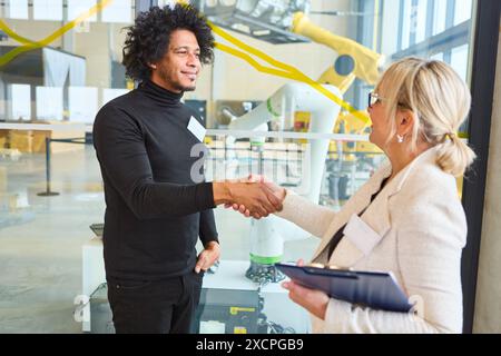 Two business professionals shaking hands with a robot in the background, symbolizing collaboration and innovation in the robotics industry. Stock Photo