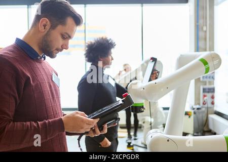 Engineers working on programming robotic arms in a modern industrial environment, showcasing technology and automation. Stock Photo