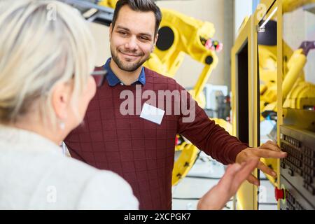 Engineers having a conversation while programming a robot. The image depicts teamwork and technology in an industrial setting. Stock Photo
