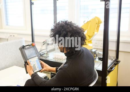 Engineer working on programming an industrial robot using a control panel in a modern laboratory setting. Stock Photo