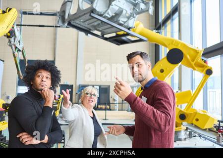 A diverse team engages in discussion about robotics and automation processes in a modern industrial environment with robotic arms and machinery. Stock Photo