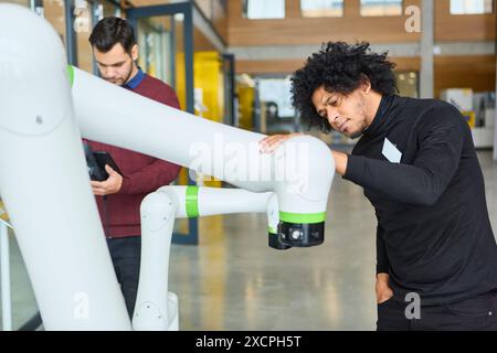 Two engineers programming and inspecting a robotic gripper arm, emphasizing industrial automation and robotics development in a modern workspace. Stock Photo