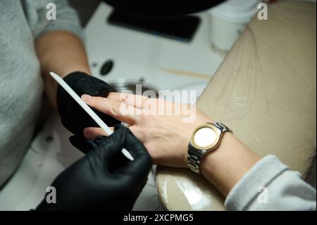 A beautician files a woman's nails during a manicure session in a beauty salon. Professional nail care and personal grooming. Stock Photo