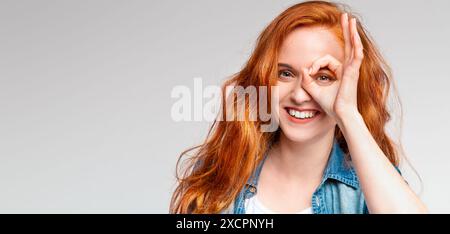 Red-Haired Woman in Denim Jacket Making OK Sign Over Eye Stock Photo