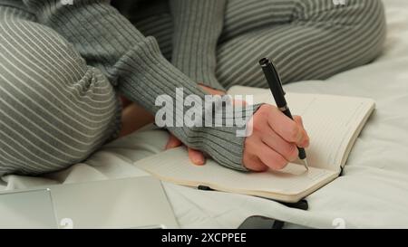 Unrecognizable student girl female lady freelancer woman businesswoman at home bedroom on bed working online write task writing in notebook notes Stock Photo