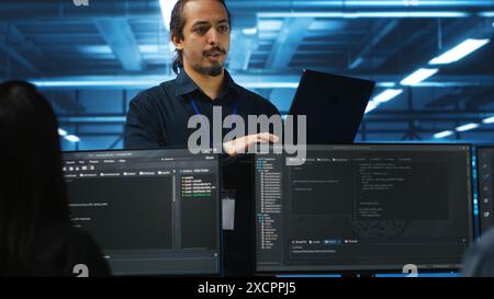 Manager in data center doing annual system review, checking parameters on laptop. Supervisor overseeing server clusters housing developed storage infrastructure used for workloads Stock Photo