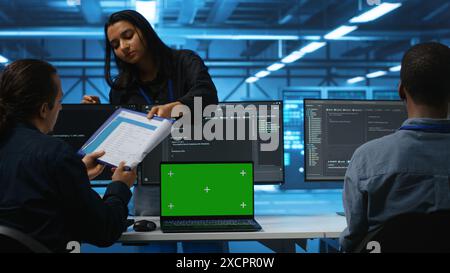 Green screen laptop in data center in front of manager and IT support specialists working together, supervising server rows. Team leader and employees overseeing supercomputers using mockup notebook Stock Photo