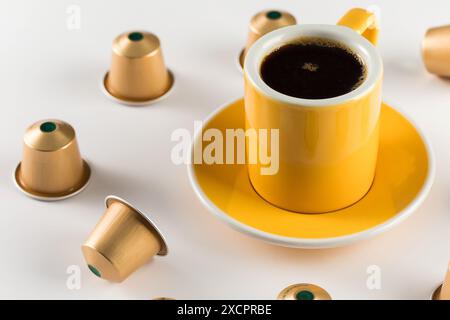 Yellow coffee cup with golden coffee capsules on a white background. Stock Photo