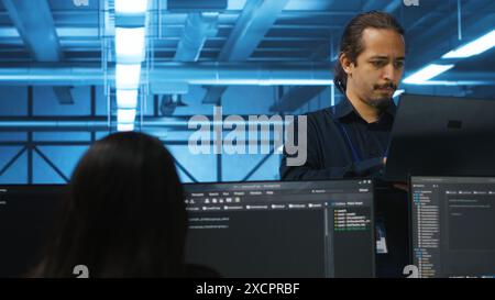 Portrait of smiling manager using laptop, supervising team in server hub providing computing resources for workloads. Happy team leader oversees engineers in data center mending supercomputers Stock Photo
