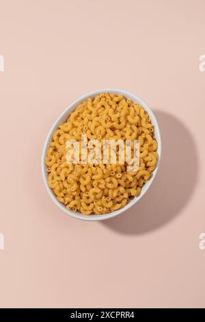 Top view of elbow macaroni pasta in a bowl on a pink background Stock Photo