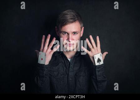 Confident tricky gambler with aces up sleeves. Illusionist showing tricks with playing cards isolated on dark background. Gambling games, luck and del Stock Photo