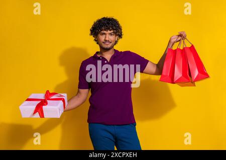 Photo portrait of handsome young man hold gift shopping bags dressed stylish violet garment isolated on yellow color background Stock Photo