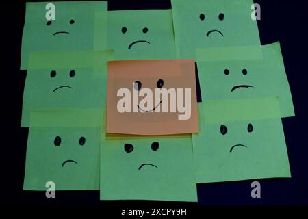 One smiley face amongst all the sad faces drawn on sticky notes. Stock Photo