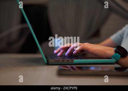 Close-up of hands typing on a laptop keyboard, with a smartwatch visible on the wrist. Indoor setting with a cozy atmosphere. Stock Photo
