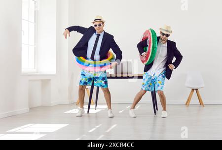 Two happy friends ready for summer holiday dancing with inflatable rings in office Stock Photo