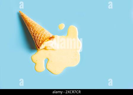 Ice cream waffle cone with melted yellow mango ice cream on pastel blue background. Minimalistic creative summer food concept design. Stock Photo