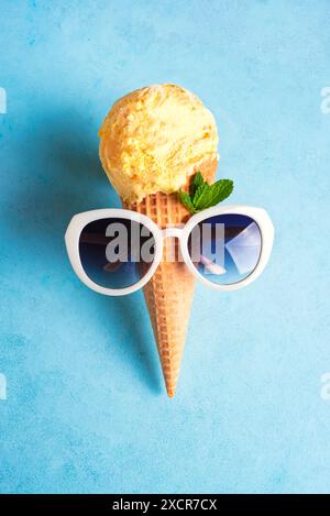 Summer creative concept with yellow ice cream cone and sunglasses on ice blue background. Trendy beach relax and summer vacation theme. Stock Photo