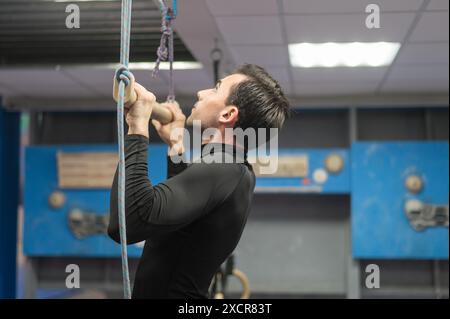 Caucasian man doing pull-ups on trapeze. Warm-up before the climbing wall.  Stock Photo