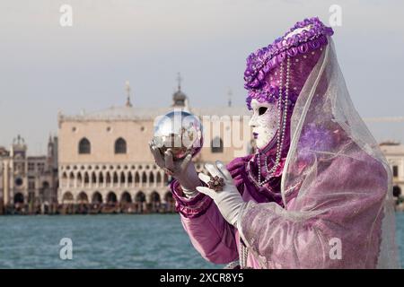 Lady in historic costume  posing in front of Doges Palace holding silver orb reflecting San Giorgio Maggiore, Venice,Italy during  Venetian Carnival Stock Photo