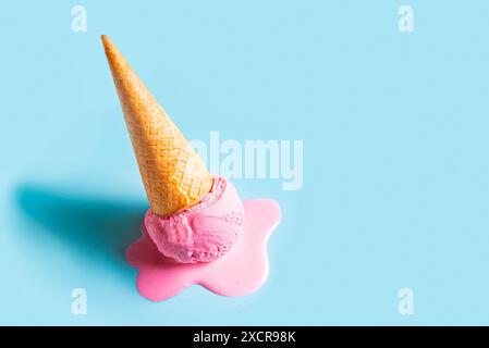 Pink ice cream melting and spilling from the waffle cone on pastel blue ...