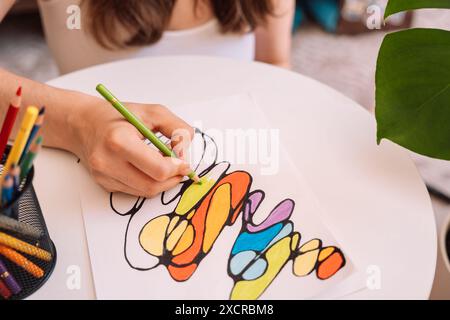 Lady paints over a drawing on a white sheet with colored pencils Stock Photo
