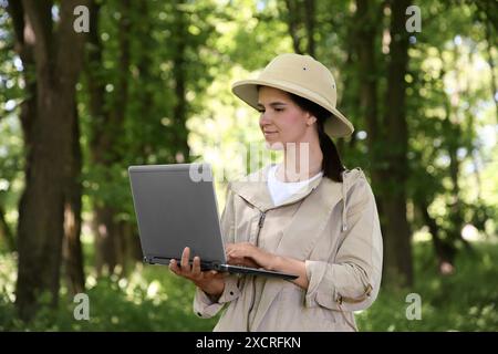 Forester with laptop examining plants in forest Stock Photo