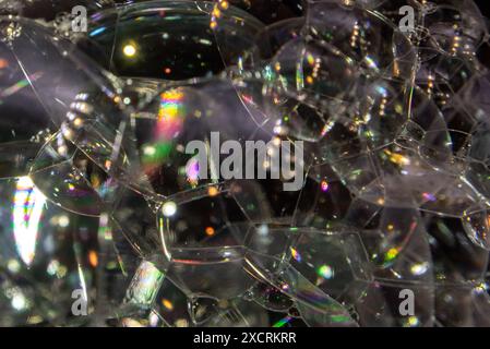 Abstract macro close up of bubble blowing multiple small bubbles with black background and colorful shapes and reflections. Stock Photo