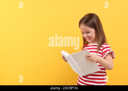 Cute little girl reading book on orange background. Space for text Stock Photo