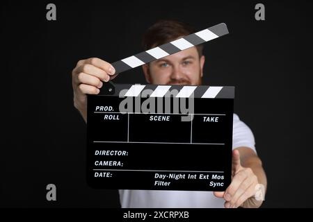 Making movie. Man with clapperboard on black background, selective focus Stock Photo