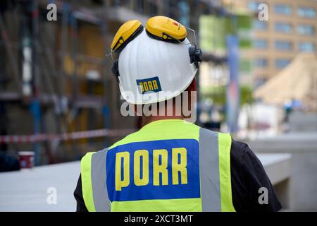 Ein Arbeiter der Firma Porr in Rückenansicht auf einer Baustelle. Er trägt eine gelbe Warnweste und einen weißen Helm mit Gehörschutz. Veröffentlichun Stock Photo