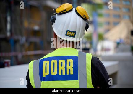 Ein Arbeiter der Firma Porr in Rückenansicht auf einer Baustelle. Er trägt eine gelbe Warnweste und einen weißen Helm mit Gehörschutz. Veröffentlichun Stock Photo