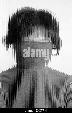 A monochrome portrait of a shy Asian woman behind a corrugated glass front Stock Photo