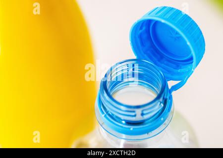 A close-up shot of an open tethered blue cap of a clear plastic bottle against a vibrant yellow background, compliance with EU environment 2024 Stock Photo