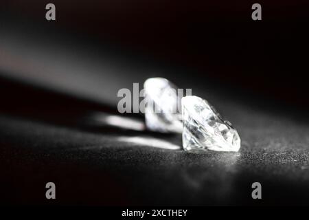 Two luxurious brilliant cut diamonds lie elegantly on a dark surface, illuminated subtly to enhance their striking clarity, intricate facets, luxury Stock Photo