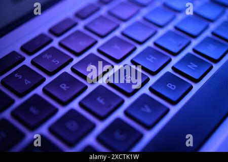 A dimly lit keyboard glows in eerie green, evoking a hacker's den. Keys with data breach alerts, malware codes, and security exploits, tense scene Stock Photo