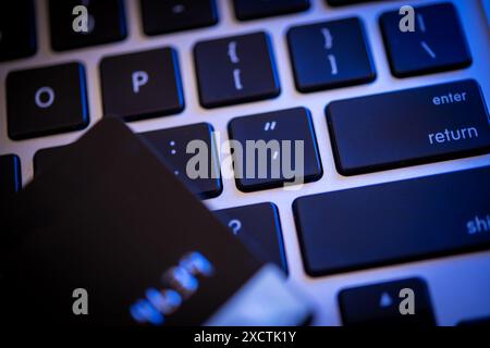 A credit card rests on the keys of a backlit computer keyboard, illustrating themes of cyber security, identity theft, and financial safety online. Stock Photo