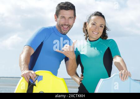 happy couple with boogie-boards making hang loose gesture Stock Photo