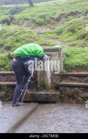 Pilgrim walking the Camino de Santiago the way of St James taking a drink from a water fountain on the route Napoleon over the Pyrenees Stock Photo