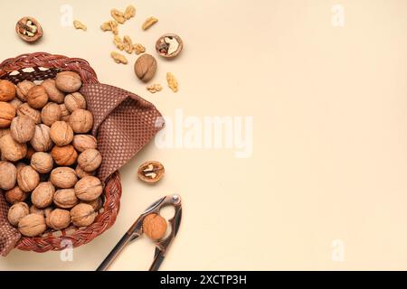 Wicker basket with walnuts and nutcracker on yellow background Stock Photo
